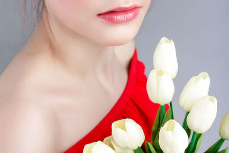 large portrait of a beautiful young girl with white tulips. Lips in the frame . Spring flower. lips with lip gloss. A lipstick kiss. no faceの写真素材