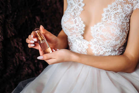 jar of perfume in the hands of the bride. Beautiful wedding manicure.Hands closeup. Wedding morning bride.white lace dress, beautiful necklineの写真素材