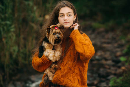 a girl on a walk with a dog in the woods, she with long hair, in an orange sweater and red tights in the fresh airの写真素材