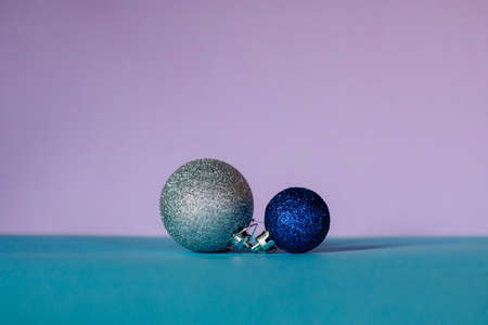 Christmas balls in blue and silver colors of different sizes are arranged in a row on a turquoise and pink background.の写真素材