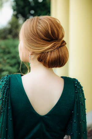 A female hairstyle is a low bun on a red-haired girl back view . Evening hairstyle, wedding...