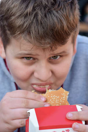 Full face portrait of young boy taking bite of fast food hamburgerの写真素材