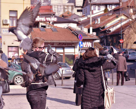 Sarajevo, Europe, 09.02.2018. Young couple feeding and playing with city pigeons on a squareのeditorial素材