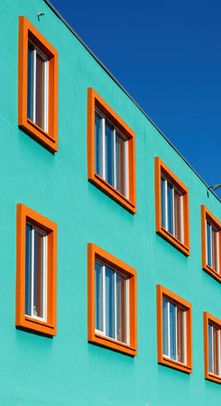 Facade of a modern apartment building with orange windows and blue skyの素材