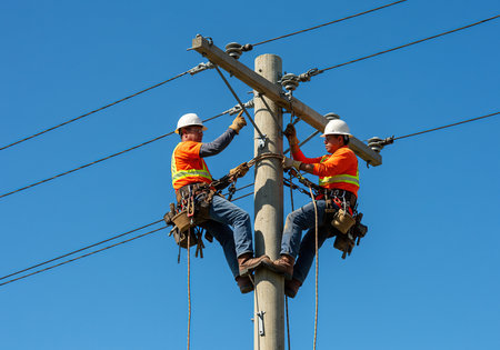 Electricians working on a high voltage power line with blue sky backgroundの素材