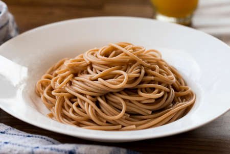 Cooked whole wheat pasta without sauce on wooden table in white plate. Spaghetti with healthy quinoa...