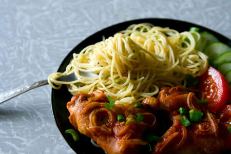 A plate with chicken wings, spaghetti and pieces of tomatoes and cucumbersの写真素材