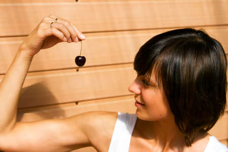 Beautiful young woman looking on a cherry with desireの写真素材