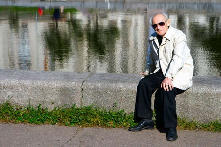 portrait of the old serious man sitting alone near the riverの写真素材