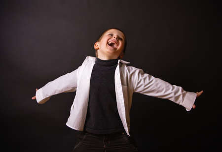 laughing boy standing with open arms against a black backgroundの写真素材