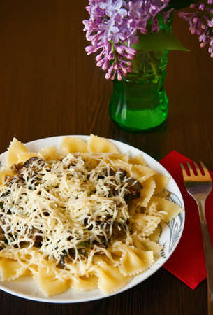 italian lunch - farfalle pasta with sause made of eggplants and served with cheese, and green vase with lilacの写真素材