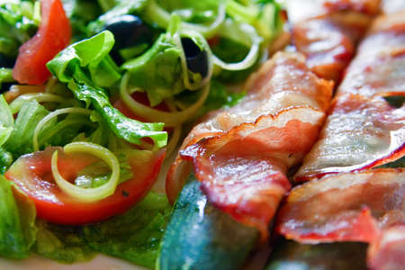close-up vegetable marrow wrapped in bacon, and salad made of tomatoes, lettuce, onion and black olivesの写真素材