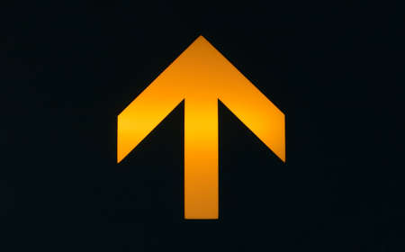 illuminated orange sign arrow on a black backgroundの写真素材