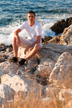 portrait of a man sitting on the rocks near the seaの写真素材