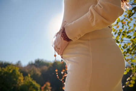 pregnant woman holding her belly, is standing in the sunlightの写真素材