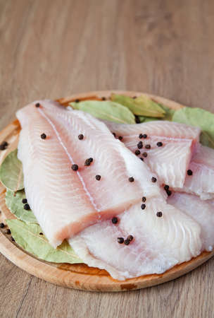 close-up raw fish pangasius with black pepper and bay leaves on a wood boardの写真素材