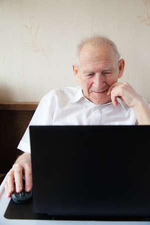 smiling old man holding computer mouse - he is working on a laptop