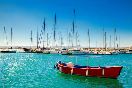 small red fishing boat in front of the big yachtsの写真素材