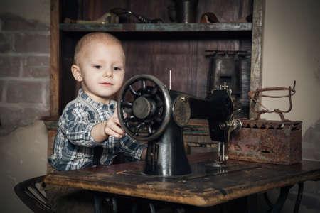 retro shot of cute little boy playing with sewing-machineの写真素材
