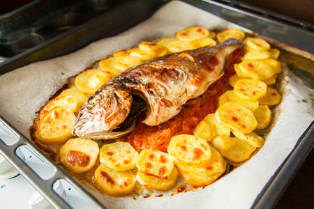 baked whole fish dorada with grilled potato, tomato and onion, on a baking tray