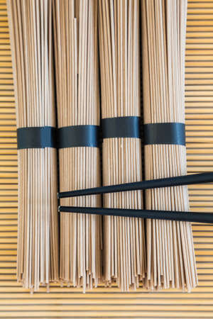 bundles of buckwheat soba noodles and black chopsticks on bamboo backgroundの写真素材