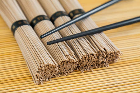 closeup bundles of soba noodles and black chopsticks on bamboo backgroundの写真素材