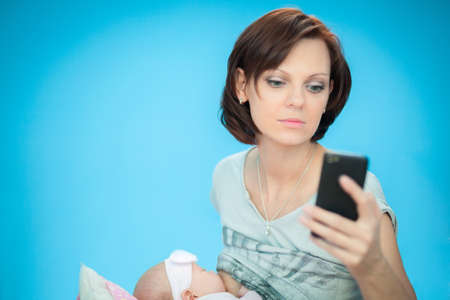 adult woman breastfeeding her newborn daughter while searching something in her smartphoneの写真素材