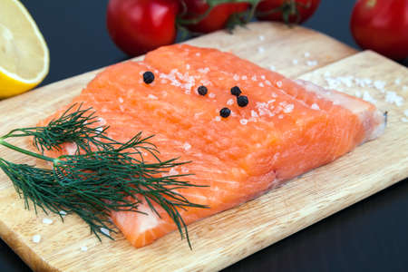 close-up raw salmon fillet with salt, pepper and dill on a wood boardの写真素材