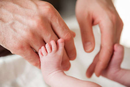 father's hands touching newborn baby's feet