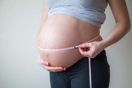 pregnant woman measuring her belly with measuring tape