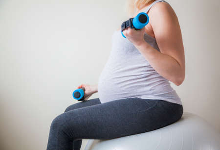 pregnant woman exercises with fitball working out with light weightsの写真素材