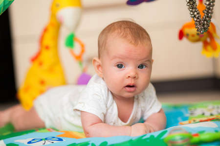 newborn baby girl lying on her belly on a play mat with toysの写真素材