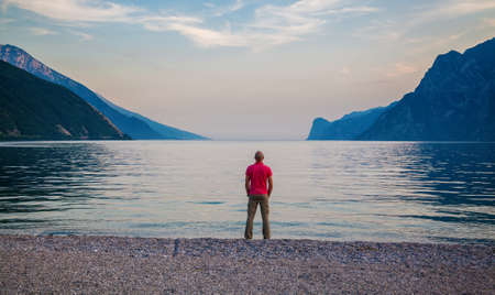 lonely man standing on the beach of beautiful Garda lake in the evening, Italyの写真素材