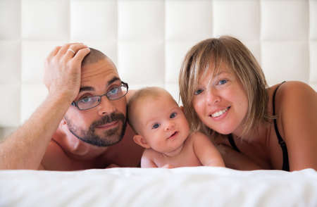 family of three - mother, father and their little baby daughter lying in a white bedroomの写真素材