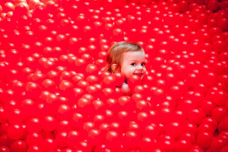 portrait of a cute little girl hiding among red plastic balls