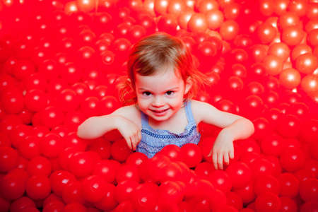 little girl having fun, playing with red plastic ballsの写真素材