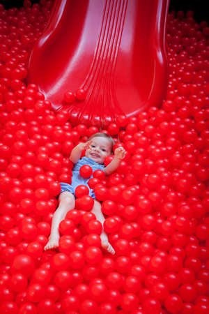 little girl riding a slide in red plastic ballsの写真素材