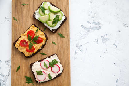 Healthy vegetarian rye bread open sandwiches with cottage cheese, hummus, avocado, raddish and...