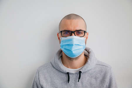 Man in glasses wearing hygienic protective mask to prevent infection such as coronavirus 2019-nCoV, indoor shotの写真素材