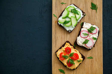Healthy vegetarian rye bread toasts with cottage cheese, hummus, avocado, raddish and tomato. Wooden...
