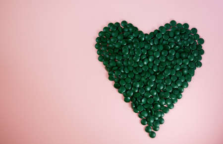 Heart made of spirulina pills on a pink background. Super food conceptの写真素材