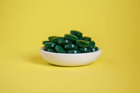 Close-up pile of green spirulina pills on a yellow background. Super food concept. Spirulina dietary supplementの写真素材