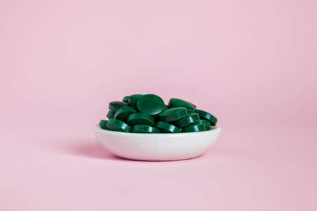 Close-up pile of green spirulina pills on a pink background. Super food concept. Spirulina dietary supplementの写真素材