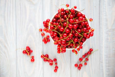 Juicy ripe fresh red currant in a white bowl on a wooden background, top view