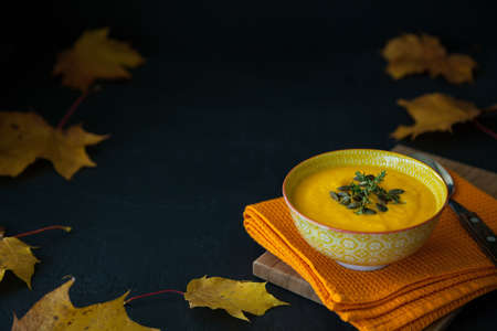 Homemade pumpkin cream soup with seeds. Yellow maple leaves on a black background.の写真素材