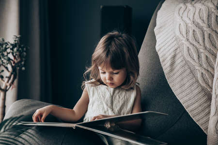 Little baby girl reading a book at home. She's isolating during quarantineの写真素材