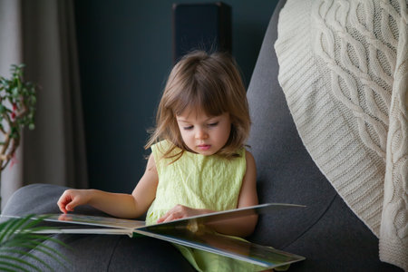 Little cute baby girl in yellow dress reading a book at home