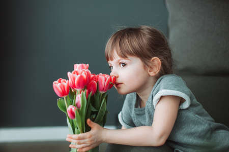 Beautiful little girl sniffing a flower of pink tulip in a vase