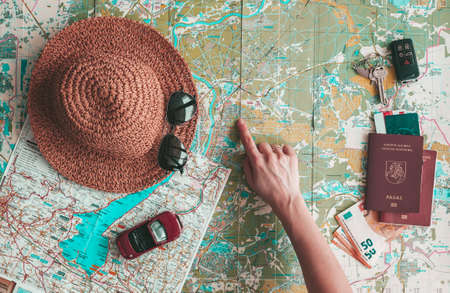 Road trip concept flat lay. Hand pointing to some place on map. Hat, sunglasses, toy car, passport, money and keys on road map background. Planning vacation.の写真素材