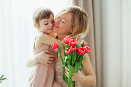 Happy mother's day! Little girl hugging her mother. Woman holding flowers. Mom and daughter smiling and spending time together. Focus on tulips.の写真素材